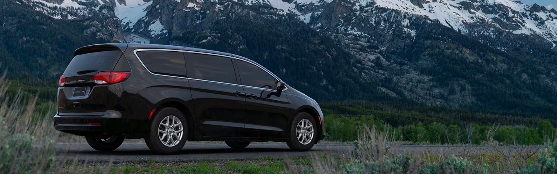 A black van sitting parked in front of some trees.