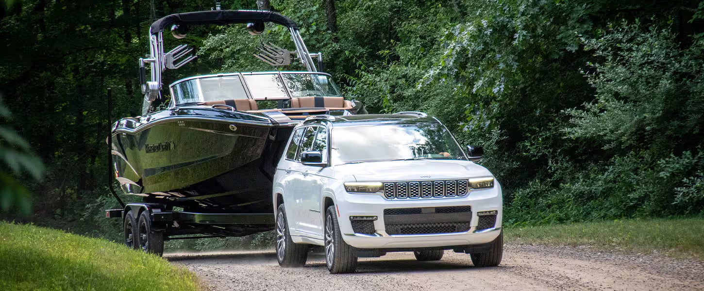 a white 2025 jeep grand cherokee towing a black speed boat on a gravel road