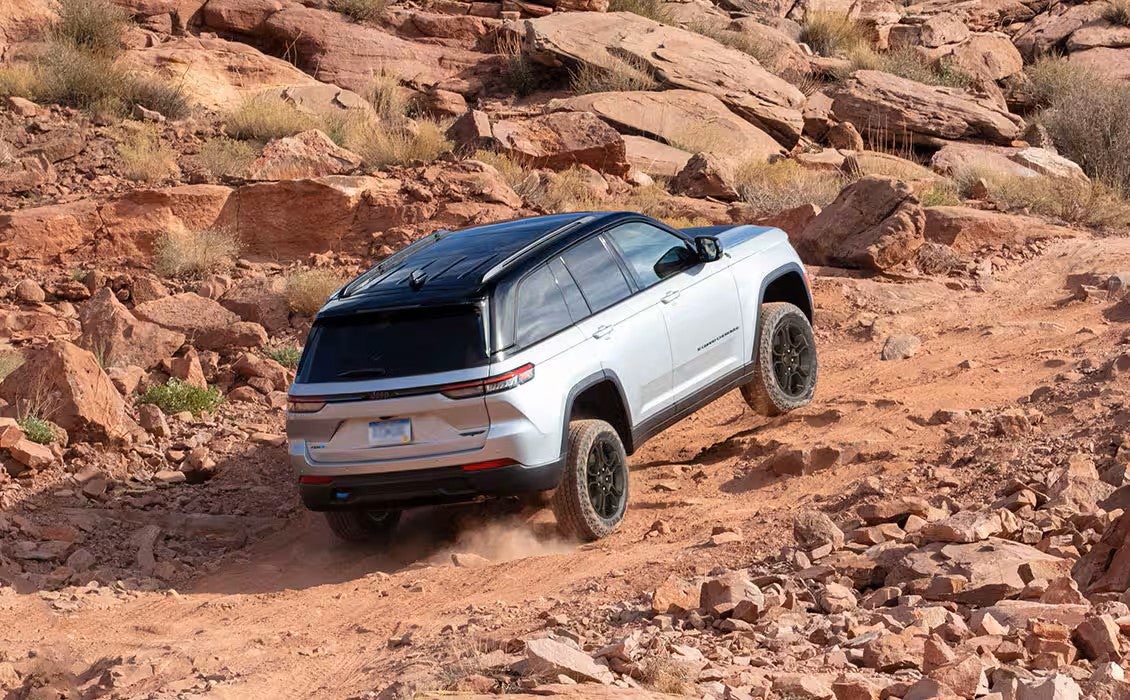 a white jeep grand cherokee driving on a dirt trail in a rocky desert terrain