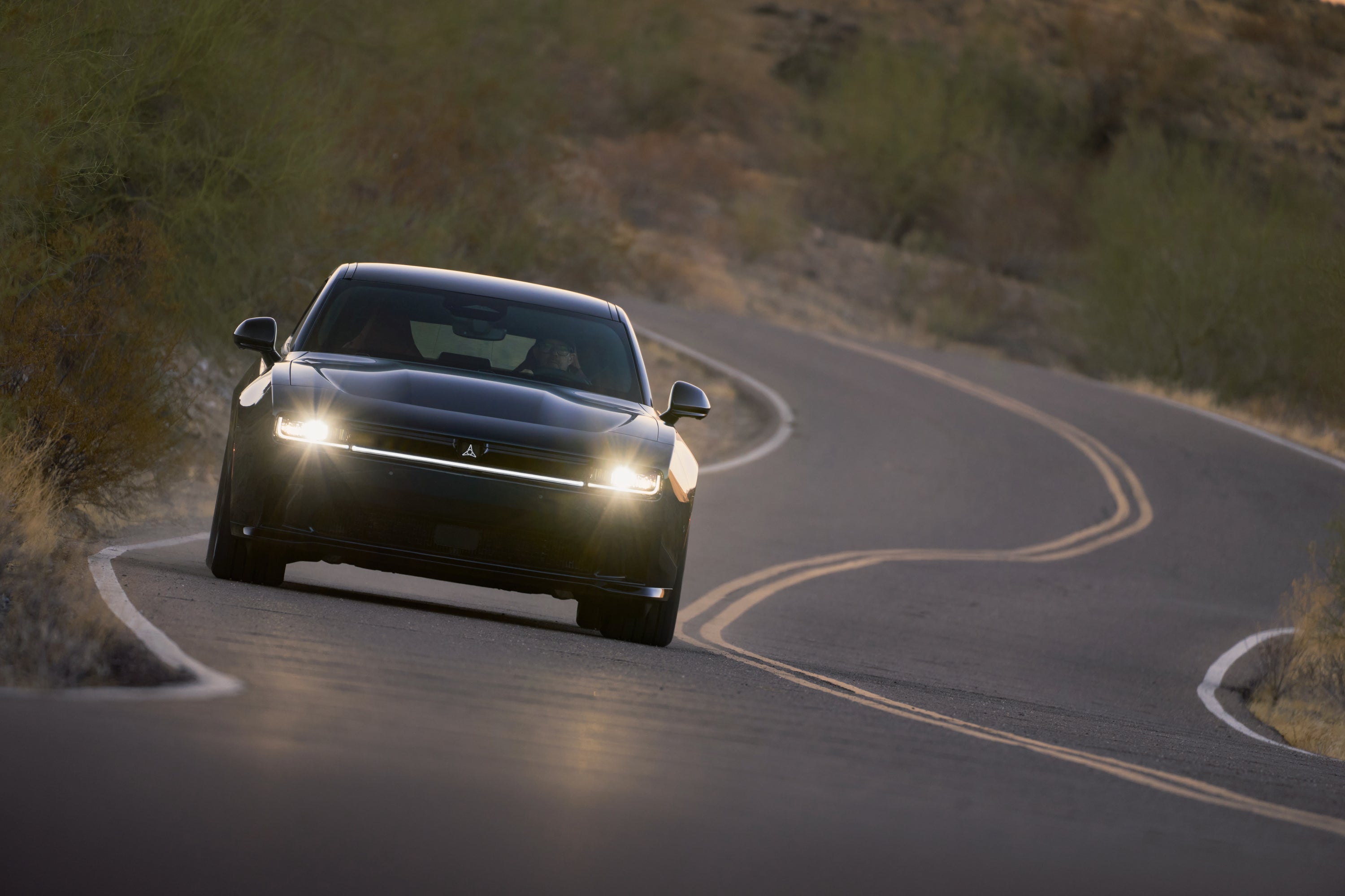 A black car driving down the road with the lights on.