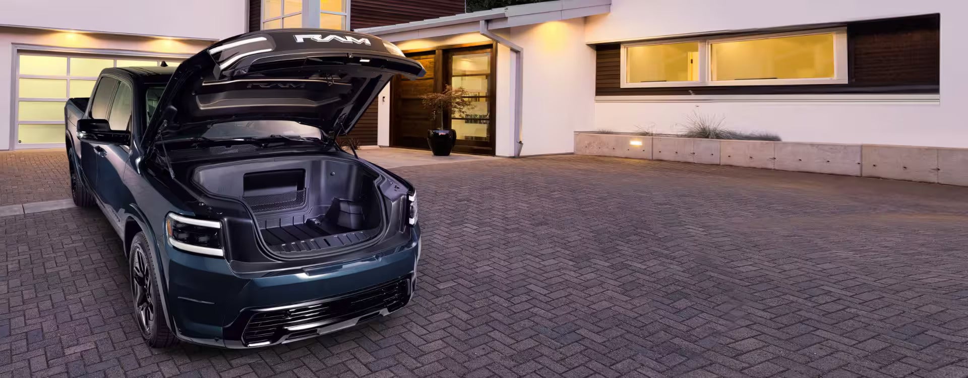 2025 Ram 1500 REV parked in a driveway with the hood open, highlighting the spacious front trunk (frunk) area for extra storage.