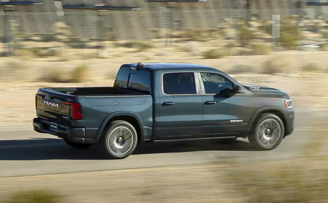 Side profile of the 2025 Ram 1500 REV driving through a desert landscape, showcasing its sleek design and powerful stance.
