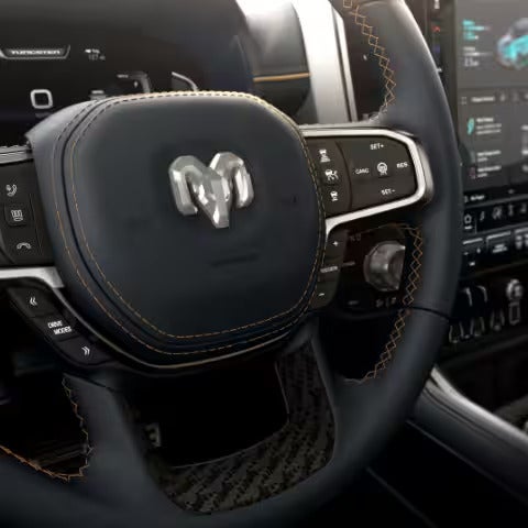 Close-up of the Ram logo on the steering wheel of the 2025 Ram 1500 REV, highlighting the detailed stitching and premium materials.