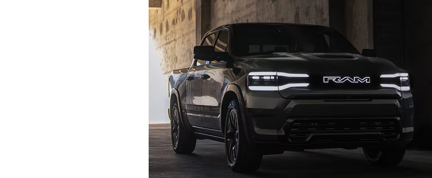 2025 ram 1500 rev truck parked in an alley way showing headlights iluminated with the RAM name lit up as well in the front grille.